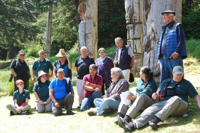 Gathering at the poles in SGang Gwaay to discuss management plans for Gwaii Haanas. Top left to right (Standing): Captain Gold, Ernie Gladstone, Jiixa Gladys Vandal, Gaahlaay Lonnie Young, Taaw.ga Halaa’ Leyga May Russ, Stiithda Frank Collison, Gitkinjuaas Ronald Wilson. Bottom left to right (Sitting): Averie Romas, Nadine Wilson, Skil Hiilans Allan Davidson, Wiigaanad Sidney Crosby, Guujaaw, Camille Collinson, Goox Laura Beaton. Photo by Council of the Haida Nation.