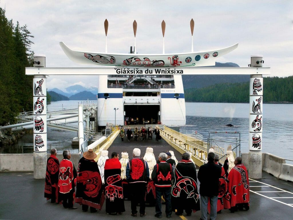 In 2011, a new ferry terminal was built to greet visitors to Klemtu. The new terminal provides a unique cultural arrival for guests. Visitors are greeted by a spectacular gateway canoe that tells the legend of the creation of Klemtu. They can rest in the cedar, crest-covered waiting building evocative of a traditional longhouse. Beautiful art adorns the welcome facilities including an imposing welcome carved pole by famed master carver Tom Hunt, a spinning salmon wind vane, concrete lock-block walls embedded with relief sculptures of salmon and herring, and a painted wood sign for Spirit Bear Lodge. Photo by Dawn Fry courtesy of Acton Ostry