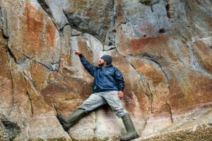 man in rain gear stands next to a cliff with ancient pictographs
