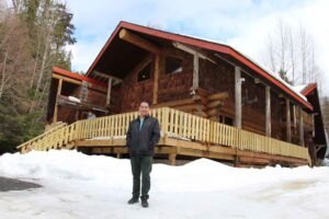 man standing in front of a renovated log cabin