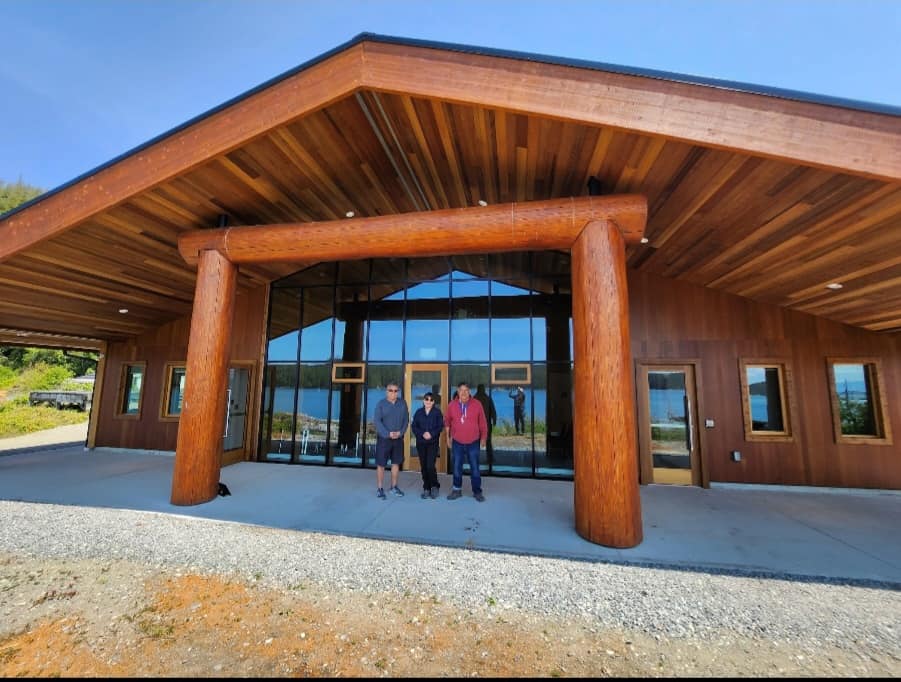 three people stand in front of a new wood-beam building