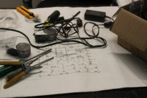 close-up of a blueprint spread out on a desk with tools and wiring scattered on top