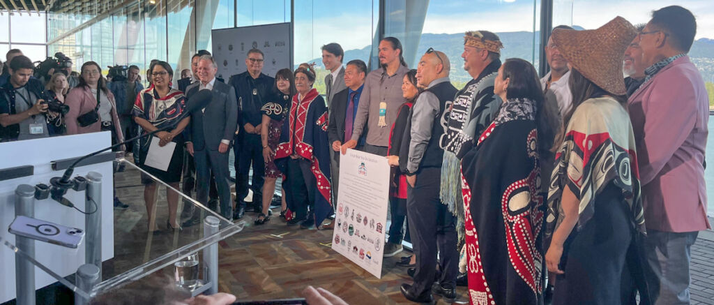 group of Indigenous leaders in regalia, as well as BC and Canadian government reps, at a press conference in Vancouver