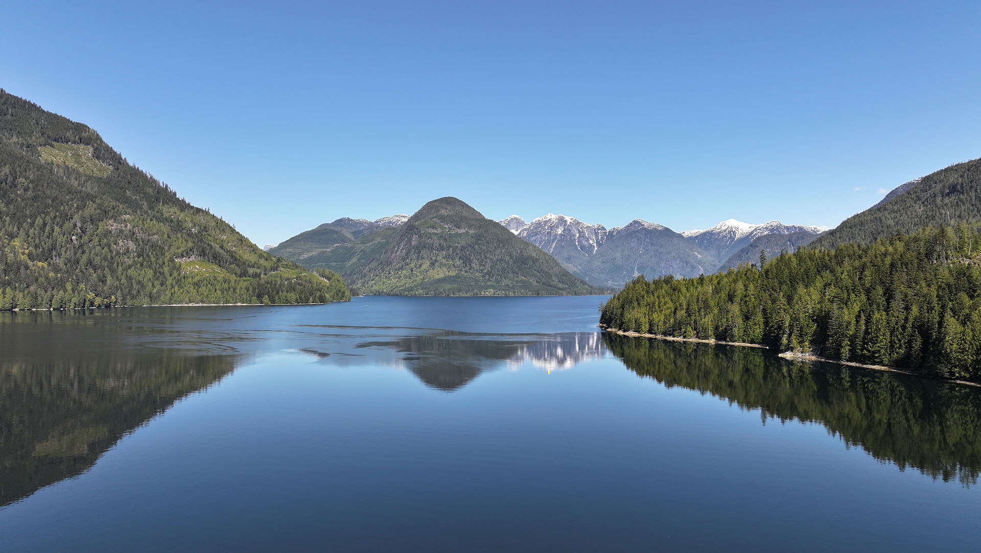 drone footage of mountains and logged forests, over a calm ocean inlet