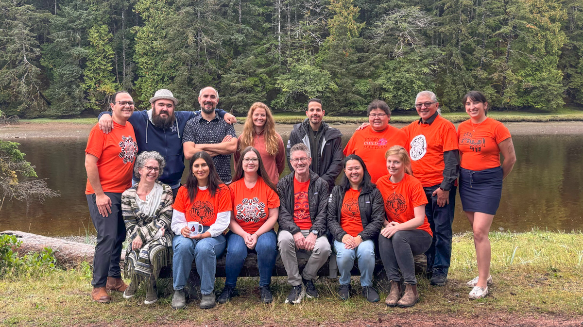 group of 14 people - many wearing orange t-shirts - pose for a group photo near a river