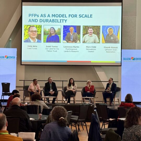 Four representatives of the PFPs in Canada sit at a panel before a large audience. The facilitator, Eddy Adra, is on one side and is directing questions to the panelists.