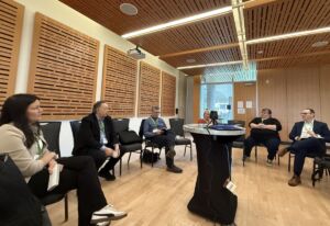 Representatives of the four PFPs in Canada gather together in a breakout room for knowledge exchange. They are seated in a circle, the room has lots of wood paneling. They are sitting relaxed and look like they are having a discussion.
