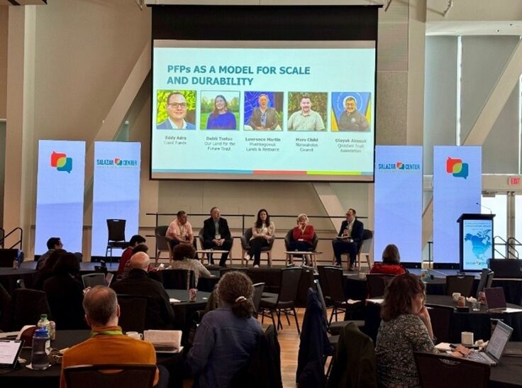 Four representatives of the PFPs in Canada sit at a panel before a large audience. The facilitator, Eddy Adra, is on one side and is directing questions to the panelists.