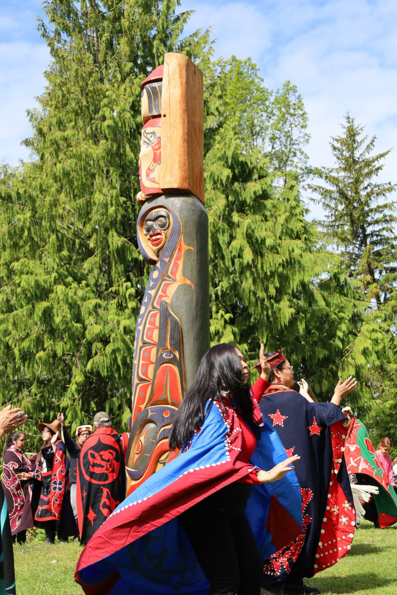 Mamalilikulla members wearing red and black regalia dance around a newly-unveiled totem pole