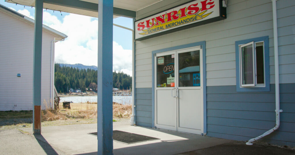 A historical photograph of Sunrise General Merchandise before renovations. The store has white and blue panelling and the logo says 'Sunrise' is bright red font.