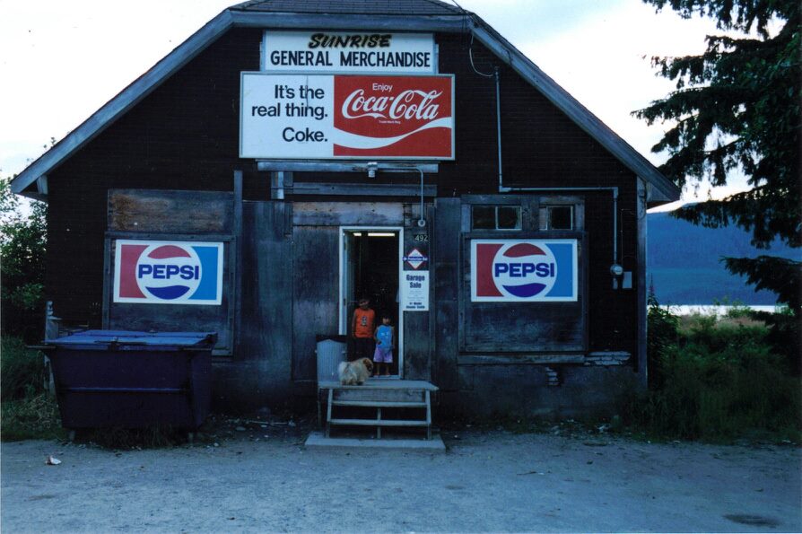An archived image of Sunrise General Store before it was torn down for renovations. The store is an old wooden structure with a large Coca-Cola advertisement taking up majority of the space.