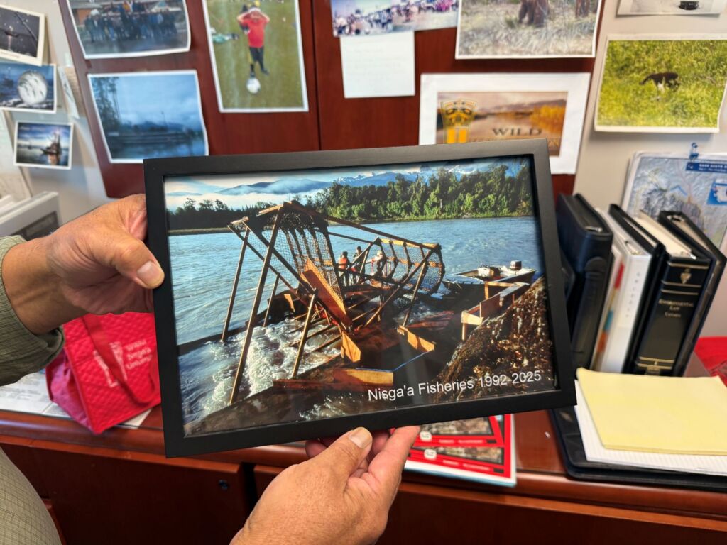 A person holds up a framed photograph which is showing off wooden fishwheels.