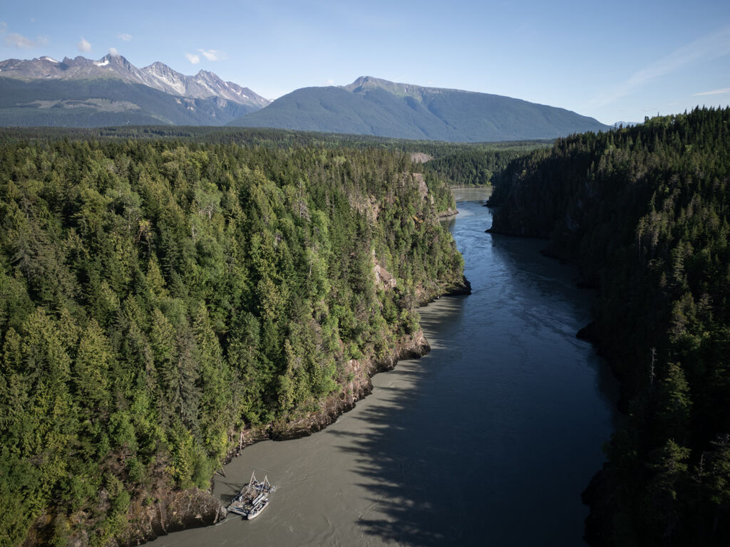 An aerial view of Ḵ’alii Aksim Lisims Nass River in an area known as Grease Harbour. The view looks at the river which is flanked by stunning mountains.