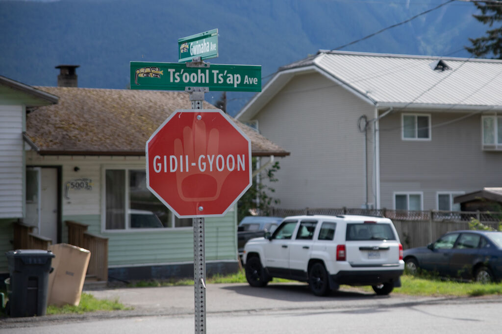 A photograph of a street in Gitwinksihlkw. At the centre, a stop sign that is depicting Nisg̱a’a language. The word says 'Gidi-Gyoon'.