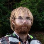 James Griffin is smiling at the camera. He is wearing a life jacket and is outdoors. James is wearing glasses and has light coloured hair.