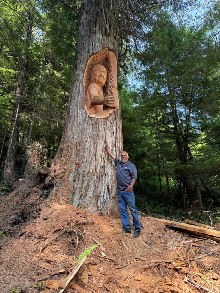 Max Chickite standing before his living tree carving representing the wild man.