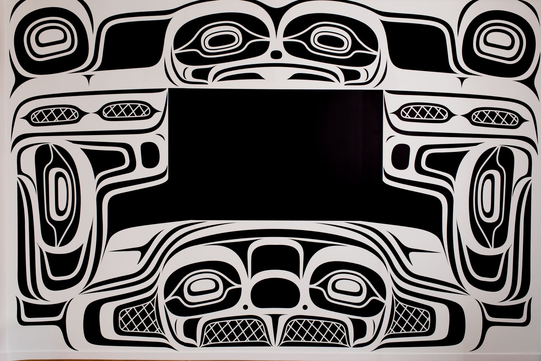 The mural is black and white, containing four beings and a number of oceanic motifs related to the story of the mural. Each formline is designed in a way to surround a TV at the centre of the wall.