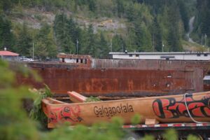A closer look at the canoe, G̱a̱lg̱a̱połala. One each side of the canoe, there is a world and a whale painted in black and red in the traditional Northwest Coast Indigenous art style.