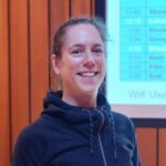 Julie is smiling at the camera. She has her hair tied back and is wearing a black zip up jacket.