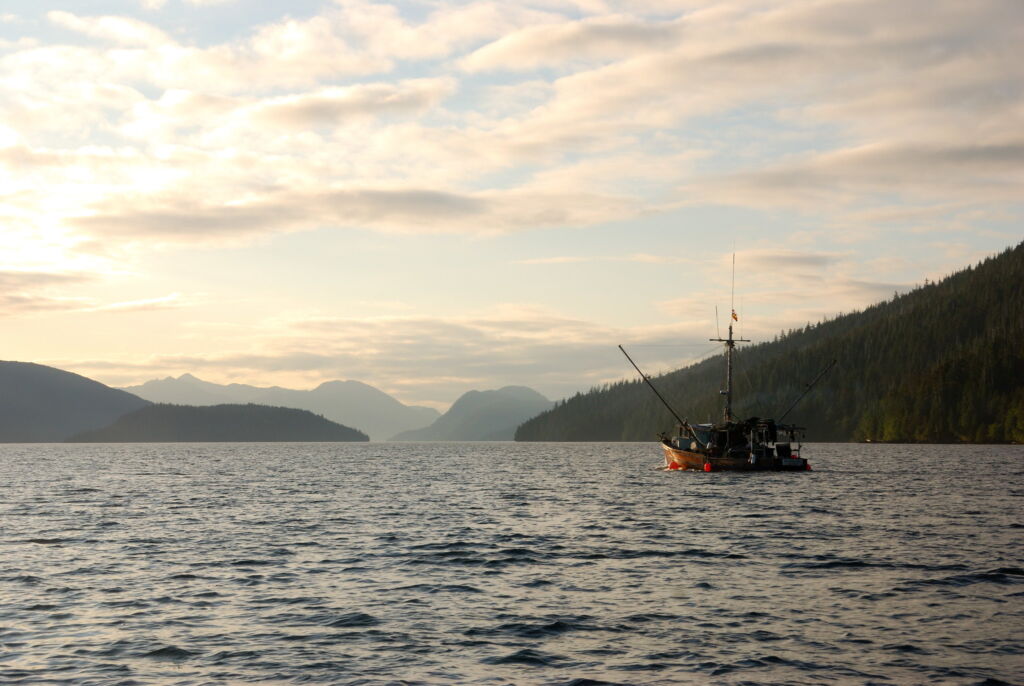 A fishing boat is far in the distance of ocean waters. Mountains can be seen beyond in the distance. 