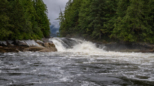 Waterfall with a large river in the foreground and clouds behind the trees
