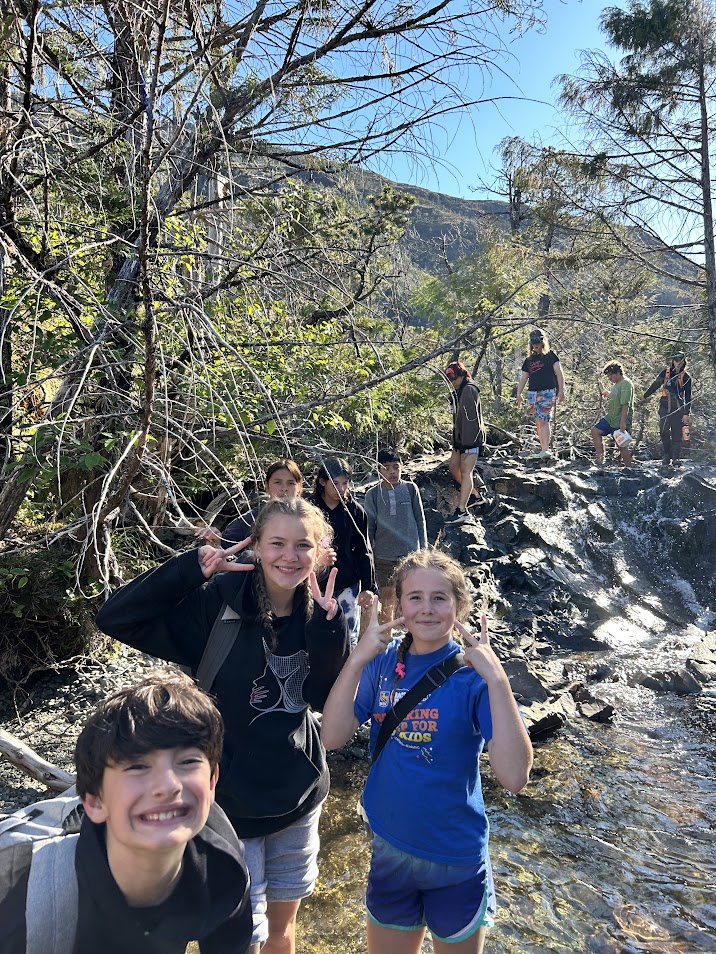 Youth participants are walking along a rocky path. In the front, they smile and pose for the camera.