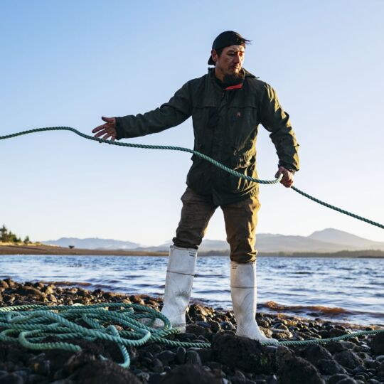 A man is working outside on a shoreline. In this action shot, he is pulling a rope and focused on a task.