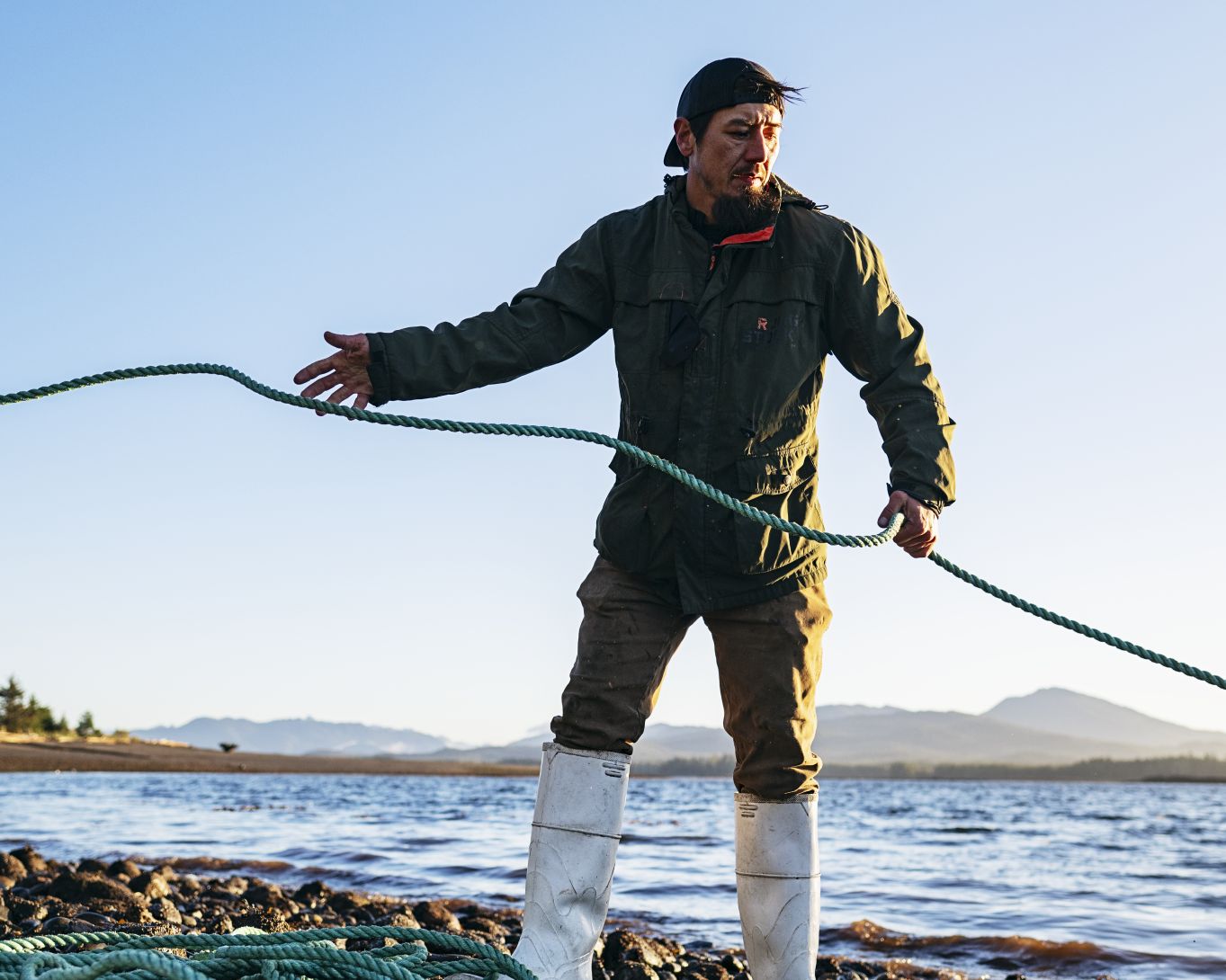 A man is working outside on a shoreline. In this action shot, he is pulling a rope and focused on a task.